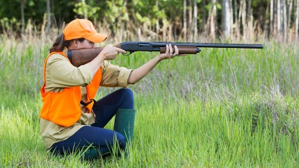 Gothaer Jagdwaffenversicherung und Sportwaffenversicherung: Jägerin mit Gewehr auf der Jagd im Wald.